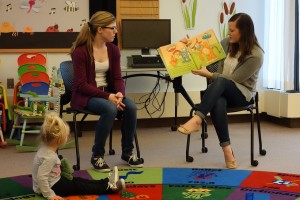 two students reading a story to toddlers