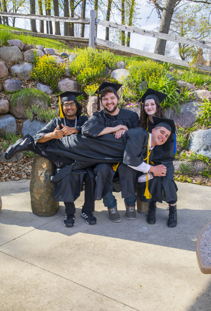 Four students posting on a bench outside in front of a rock wall. 